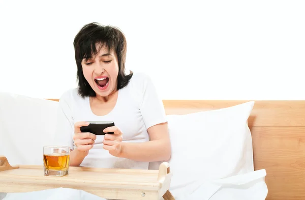 Femme joue à des jeux vidéo sur téléphone mobile au lit — Photo