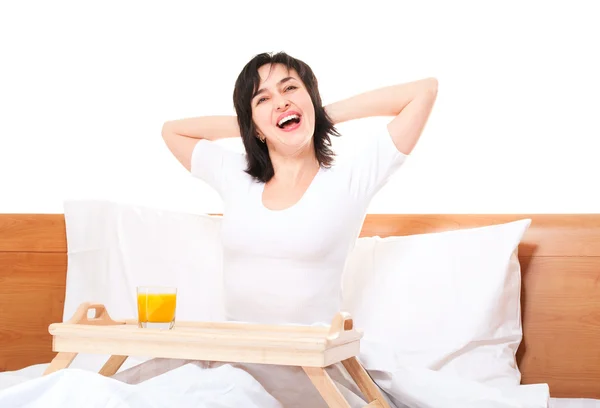 Güzel bir kadın yatakta tepsi ve turuncu bardak germe — Stok fotoğraf