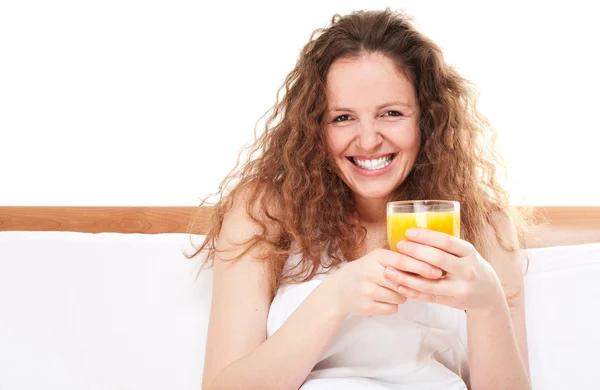 Mulher ruiva feliz na cama com copo de suco de laranja — Fotografia de Stock