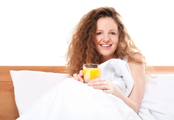 Mujer pelirroja feliz en la cama con un vaso de jugo de naranja — Foto de Stock