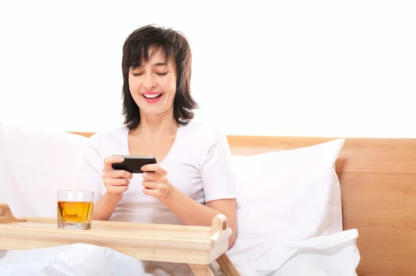 Mujer juega videojuegos en el teléfono inteligente móvil en la cama —  Fotos de Stock