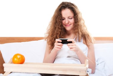 kadın yatakta cep telefonunda video oyunları oynuyor.