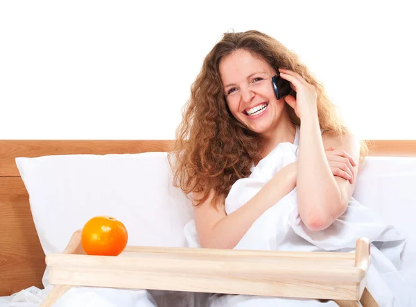 Nő az ágyban, beszélő narancs telefonon a tálca — Stock Fotó