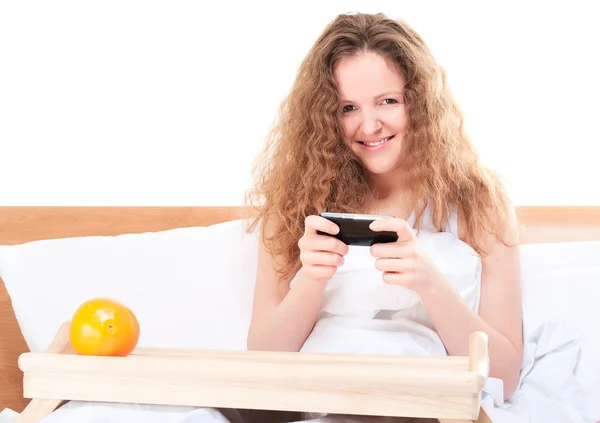 Kadın yatakta cep telefonunda video oyunları oynuyor. — Stok fotoğraf