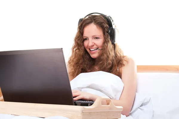 Žena s notebookem a headsetu v posteli — Stock fotografie