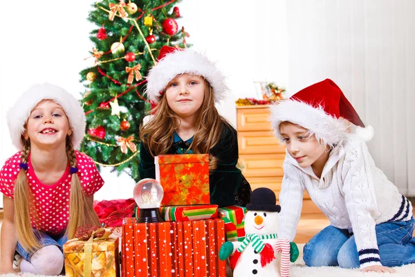 Kinder sitzen neben Weihnachtsgeschenken lizenzfreie Stockfotos
