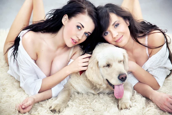 Mulheres sorridentes deitadas no tapete com o cão — Fotografia de Stock