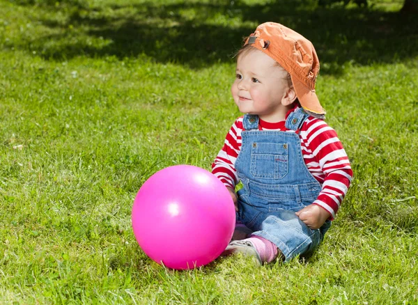 Тоддлер сидит с мячом в саду — стоковое фото