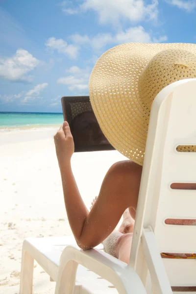 Женщина сидит на пляже и просматривает интернет с планшетным компьютером — стоковое фото