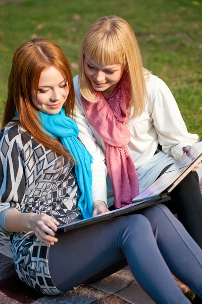 Две сестры смотрят фотоальбом в парке — стоковое фото