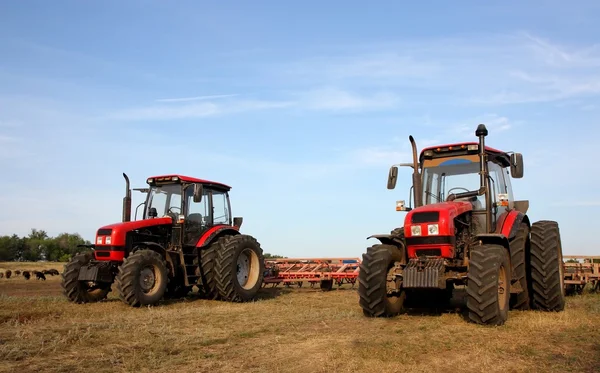 Twee rode trekkers met een harrow — Stockfoto