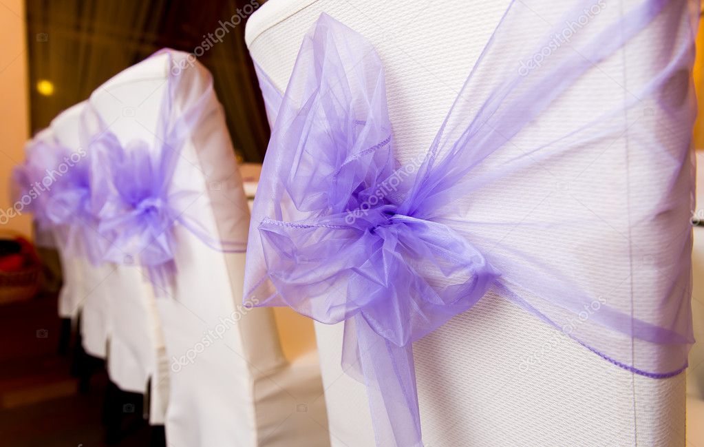 White wedding chairs decorated with purple bows