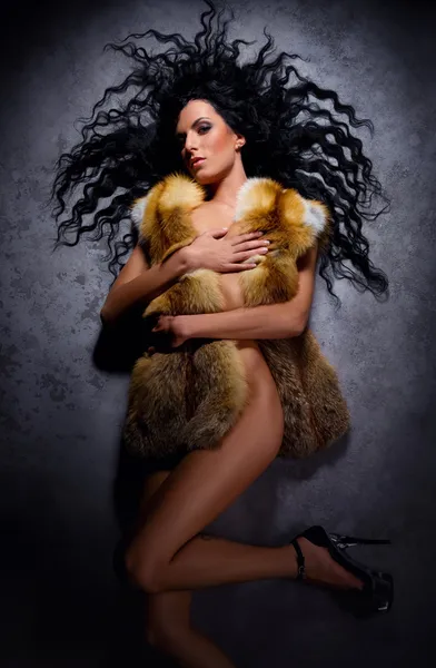 Gorgeous brunette wearing fur vest lying indoors — Stock Photo, Image
