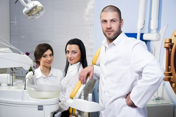 Vänliga manliga tandläkare, assistent och leende patienten på tandvårdsklinik — Stockfoto