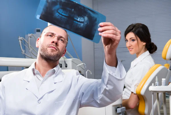 Стоматолог с рентгеном и улыбающимся пациентом на заднем плане — стоковое фото