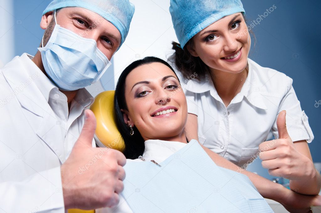 Dentist with assistant and smiling patient showing thumb up