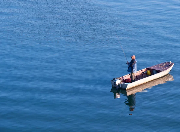 Рыбак, стоящий на лодке и рыбалка в море — стоковое фото