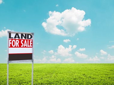 Land for sale sign on empty green field clipart