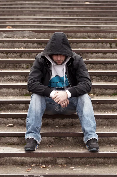 Sad teenage boy with hood sitting on stairs — Stock Photo, Image