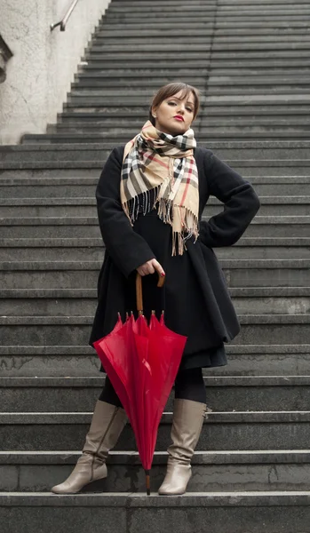 Bella donna con sguardo serio che tiene l'ombrello rosso sulle scale — Foto Stock