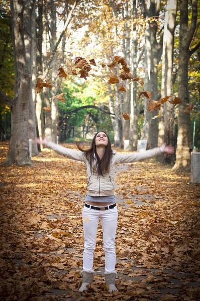 Jovem bela mulher jogando as folhas amarelas no ar em au — Fotografia de Stock