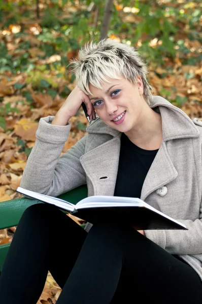 Привлекательная блондинка с короткими волосами сидит на скамейке с книгой — стоковое фото