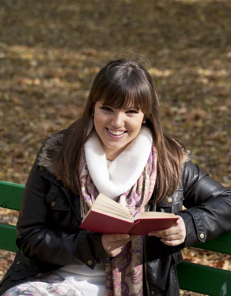 Студентка читает книгу о скамейке в осеннем лесу — стоковое фото
