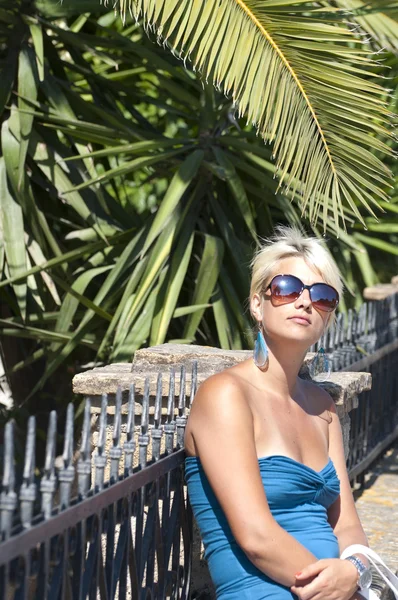 Attraente ragazza bionda con occhiali da sole in posa vicino alla palma — Foto Stock