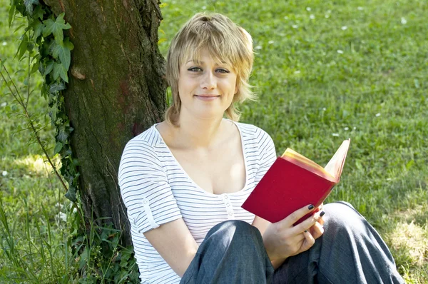 Portrait d'un étudiant souriant lisant un livre dans la nature — Photo