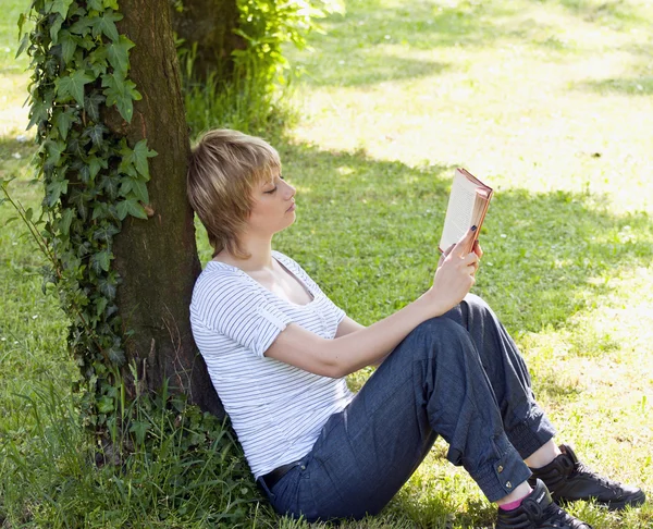 Portrait of student leaned against tree and reading book — Stock Photo, Image