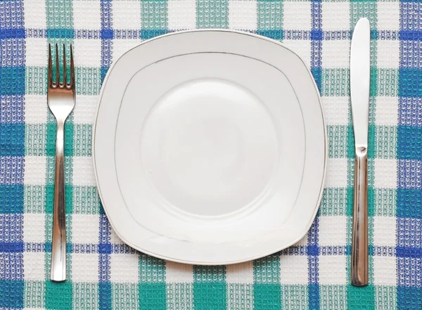 Bílý prázdný talíř s vidličkou a nožem na kostkovaný ubrus — Stock fotografie