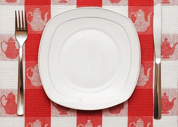 Cuchillo, plato blanco y tenedor sobre mantel rojo —  Fotos de Stock