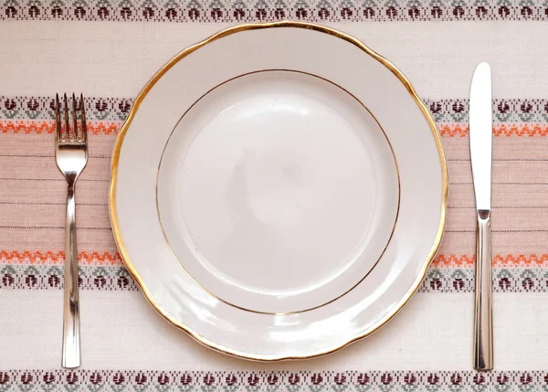 Нож, белая тарелка и вилка на скатерти — стоковое фото