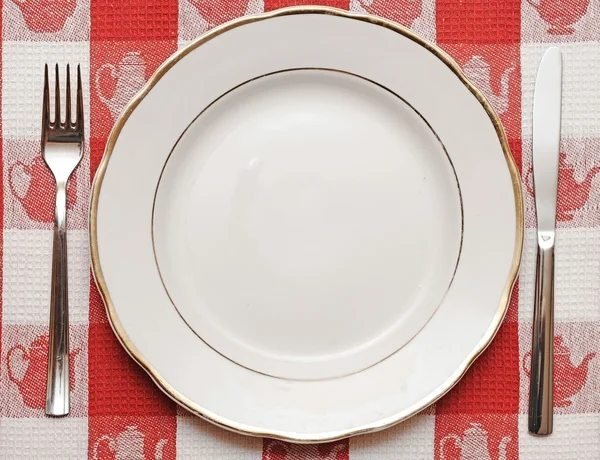 Knife, plate and fork on red tablecloth — Stock Photo, Image