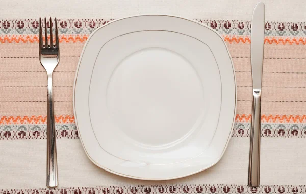 Faca, placa branca e garfo na toalha de mesa — Fotografia de Stock