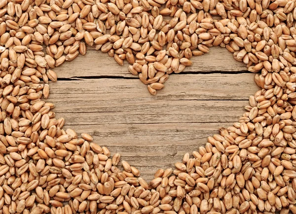 Shape of the heart is made of wheat against a wooden background — Stock Photo, Image
