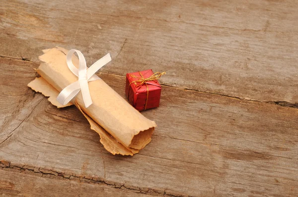 Caixa vermelha com um velho pergaminho em fundo de madeira — Fotografia de Stock