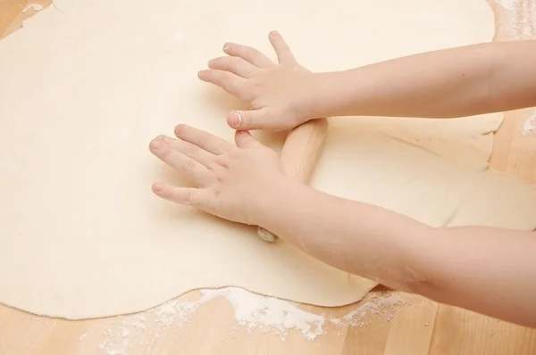 Дитячі руки замішують тісто на дерев'яному столі — стокове фото