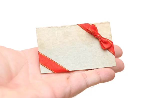 Etiqueta de presente em branco com fita vermelha e arco na mão segurando no branco — Fotografia de Stock