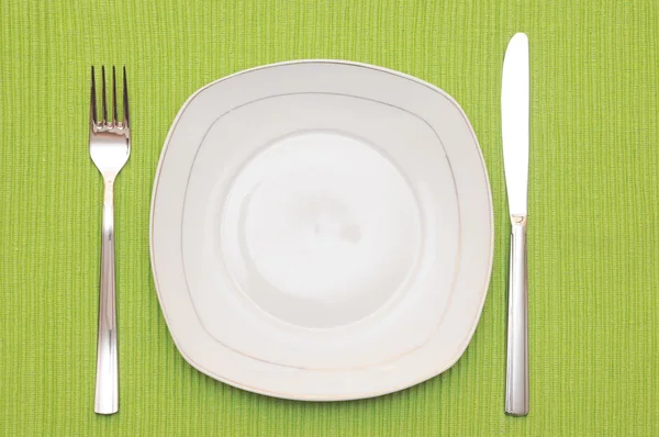 空の皿、ナイフおよびフォークおよび木製のテーブルの上の緑のナプキン — ストック写真