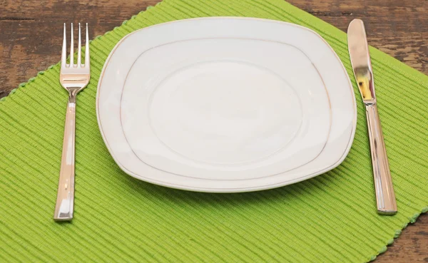 Empty dish, knife and fork and green napkin on wood table — Stock Photo, Image