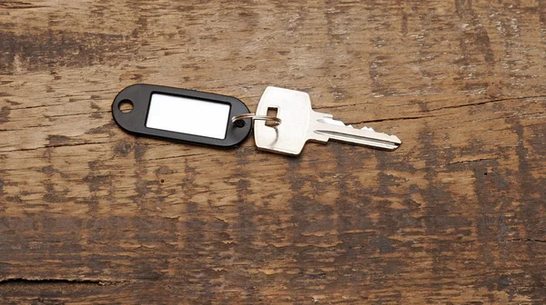 Серебряный ключ с бланшированной биркой на деревянном фоне. Space for your tex — стоковое фото