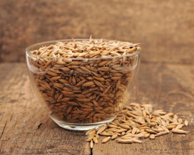 Closeup oats heaped in a glass cup on wooden table clipart