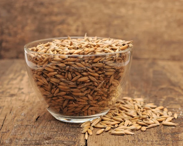 Closeup oats heaped in a glass cup on wooden table — Stock Photo, Image