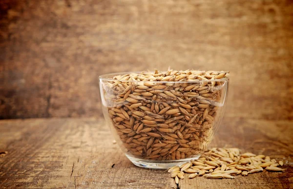 Oats heaped in a glass cup on wooden table — Stock Photo, Image
