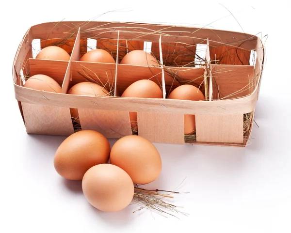 Ovos com uma palha em uma cesta de madeira em um fundo branco . — Fotografia de Stock