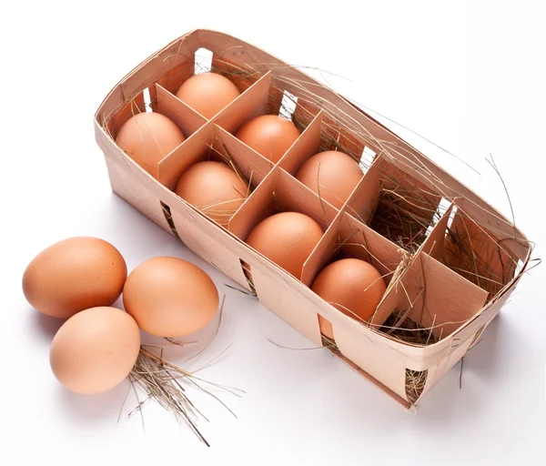 Ovos com uma palha em uma cesta de madeira em um fundo branco . — Fotografia de Stock