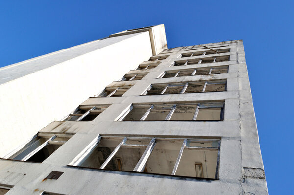 Damaged old grunge industrial building with broken windows upon blue sky