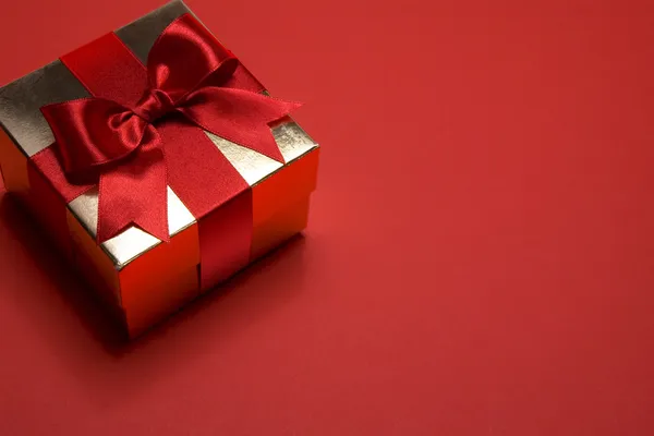 Τέχνη χρυσό δώρο κουτί με ένα κόκκινο τόξο σε κόκκινο φόντο — Φωτογραφία Αρχείου