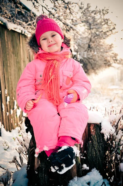 Μικρό παιδί κοριτσάκι που κάθεται σε ένα κούτσουρο σε μια μέρα του χειμώνα — Φωτογραφία Αρχείου